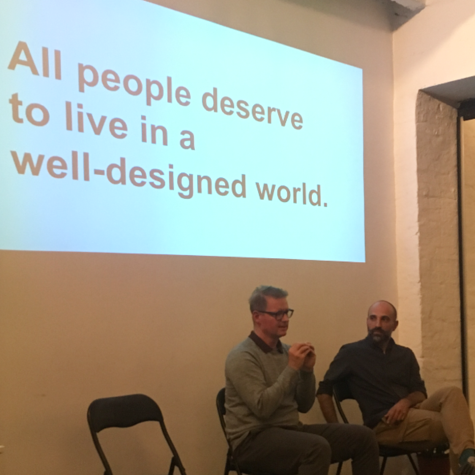 Talk session — 'All people deserve to live in a well-designed world.' projected behind two speakers.